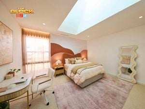 Cream bedroom with a queen bed, desk and mirror on a blush rug and a red and orange hill style bedhead.