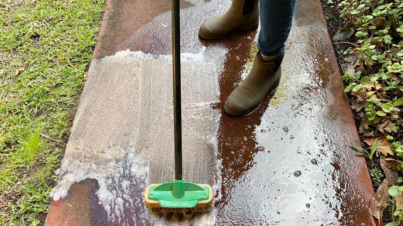 Stiff bristle brush scrubbing solution over concrete.