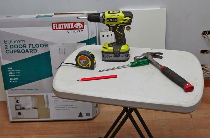 A tape measure, drill, hammer, screwdriver and pencil on a table