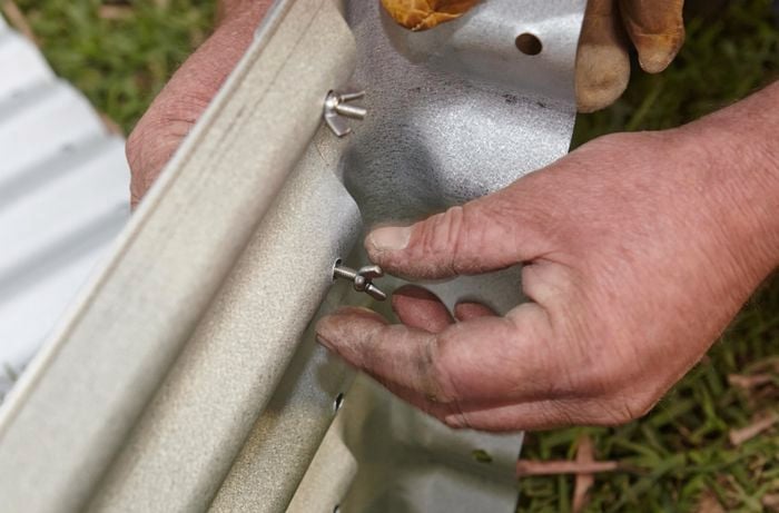 Person tightening nuts and bolts to hold corrugated iron garden bed together.