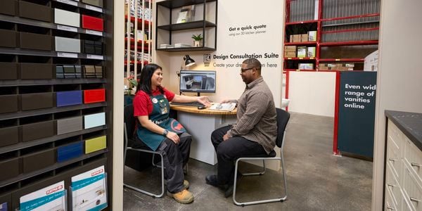 Bunnings Team Member and a customer in a store sitting at a deck with a screen and keyboard on it.