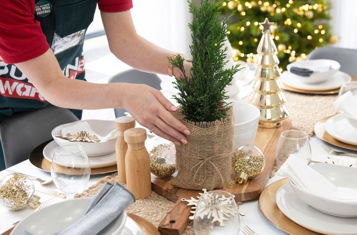 Person placing a miniature conifer tree on a table set with decorations