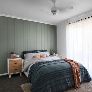 Bedroom with green wall panelling, bed, bedside table and sheer curtains.