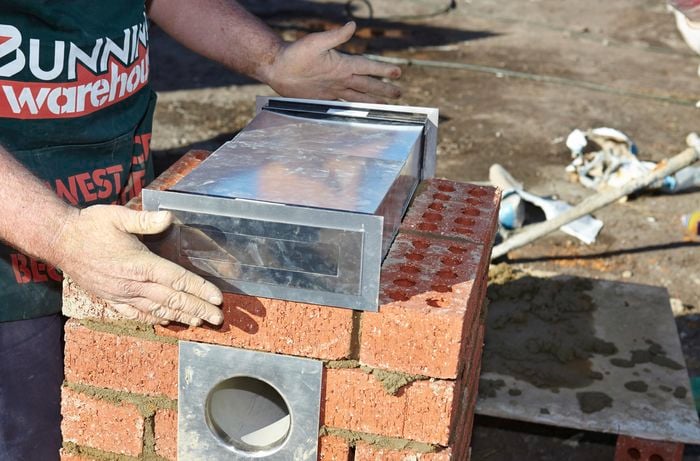 A steel mail slot being added to a middle layer of a brick letterbox