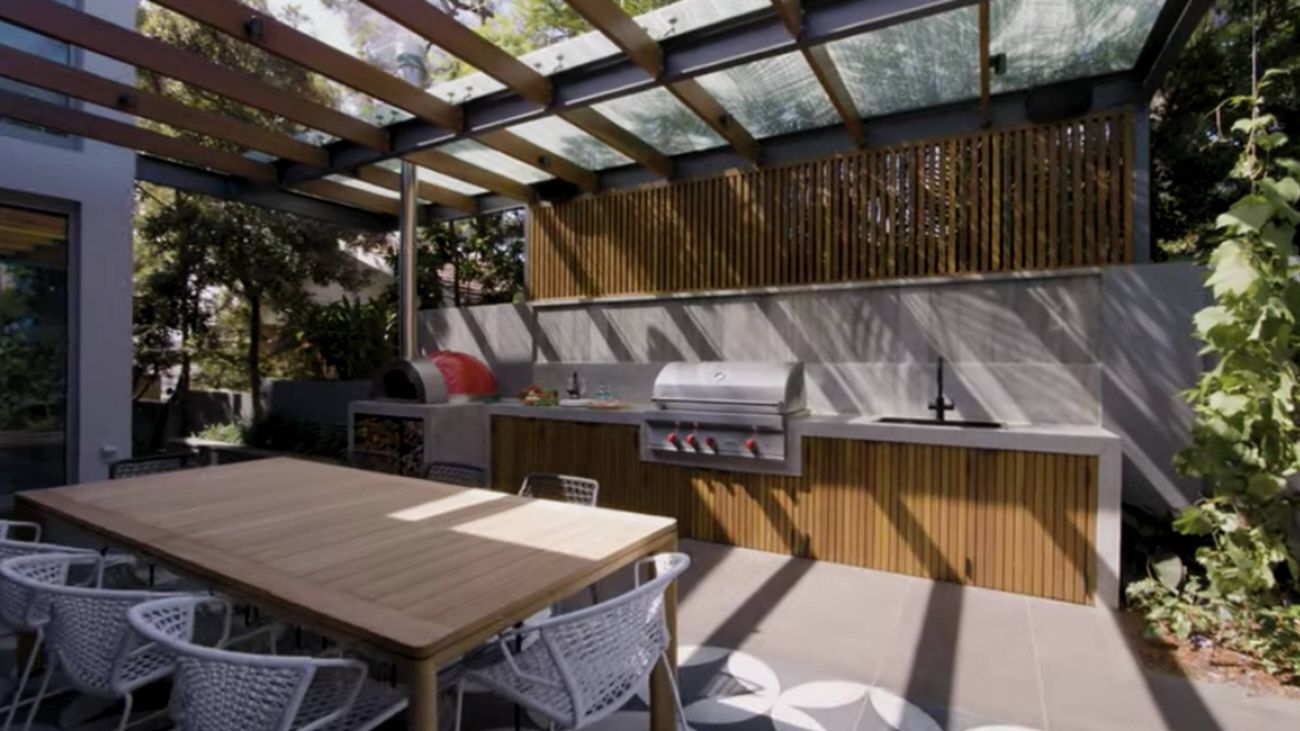 Against the back wall of an expansive patio area, a pizza oven, large barbecue and sink form a stylish outdoor kitchen