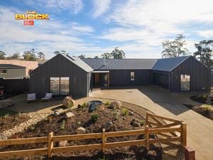 The front area of a house with rocks, shrubs, a driveway and a timber fence in it.