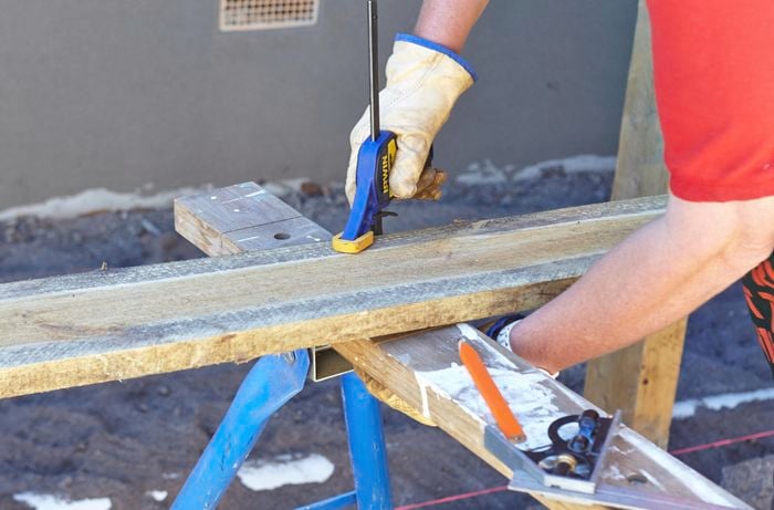 Person using clamp to secure timber plinth in place, ready for cutting.