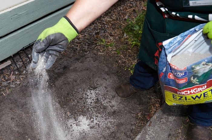 A person spreading soil wetter onto a garden bed