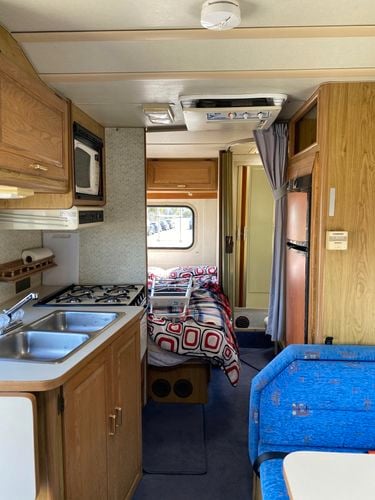 The interior of an old RV caravan with timber cabinetry and a blue couch.