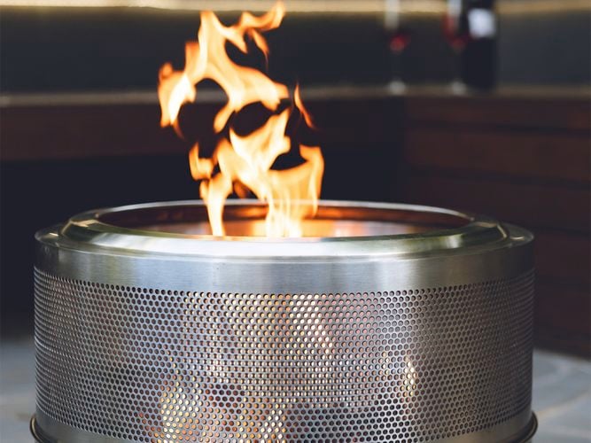 Close-up of a stainless steel Wildfire fire pit with tall flames rising from the centre, set on an outdoor tiled surface.