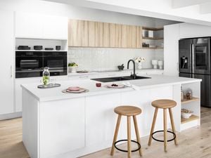 Modern white kitchen with timber bar stools and  timber feature cabinets, black sink and mixer tap and a large double door fridge.