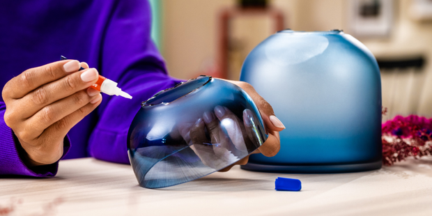 Applying glass adhesive to a blue glass vessel during a decorative repair project.