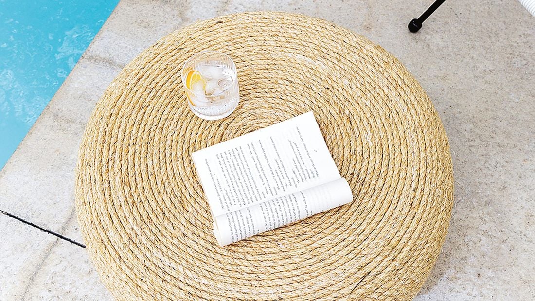 A book and a water glass on top of a nicely designed ottoman.