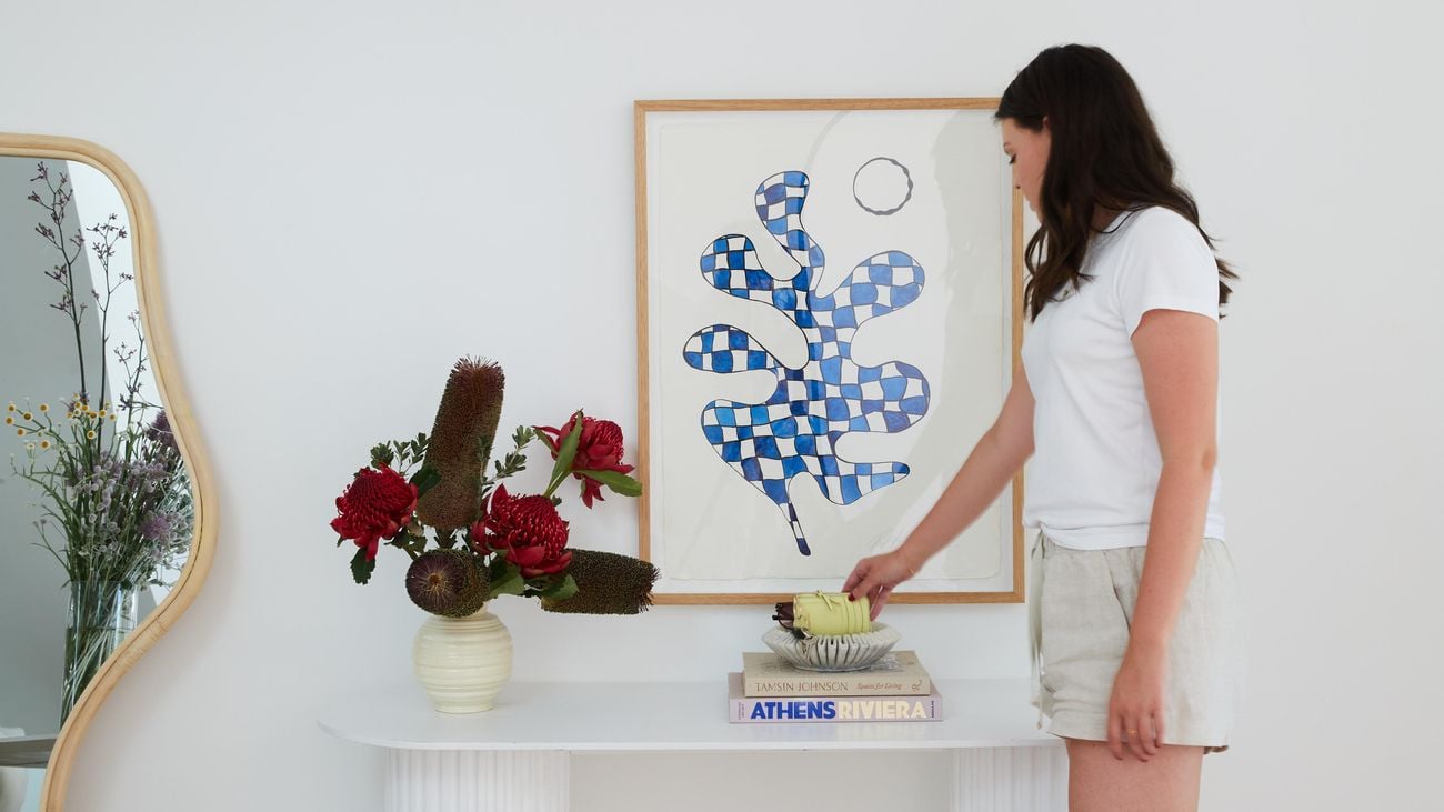 A woman stands in the front entrance of a house with a decorative table and picture sitting on top