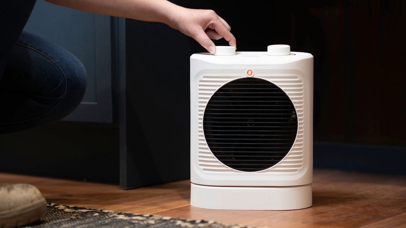 A person is adjusting the thermostat on a 2400W fan heater.