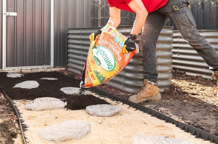 A person is spreading potting mix between the pavers and borders.