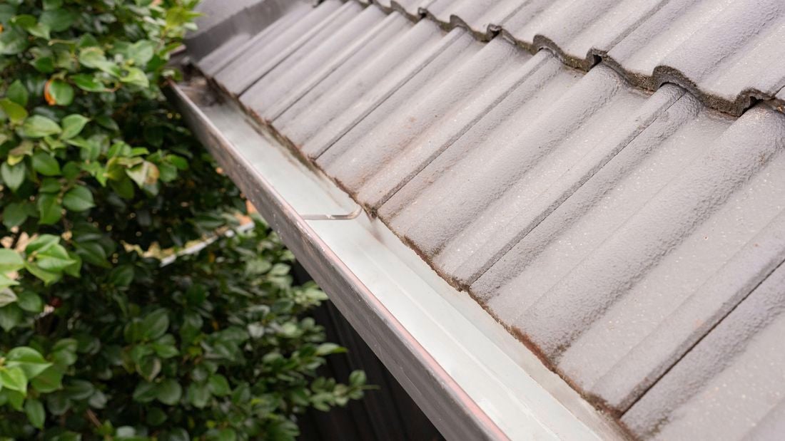 A freshly cleaned roof gutter along the edge of a house with grey tiled roofing