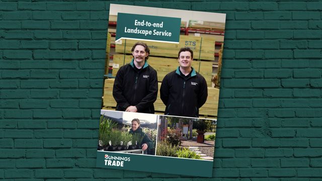 Bunnings Trade landscape services brochure displayed against a teal brick wall, featuring photos of landscaping staff, plants, timber products, and the text “End-to-end Landscape Service.