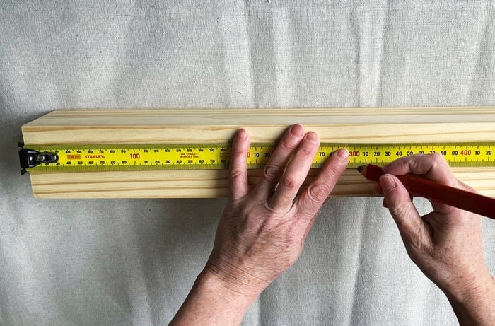 Hands holding a ruler and pencil, marking measurements on a length of timber on a drop sheet
