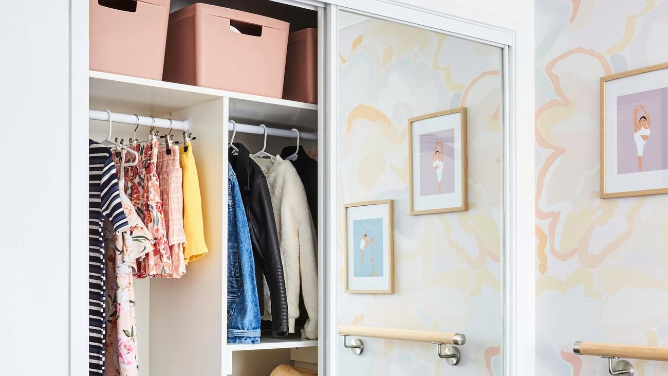 A mirrored wardrobe in a children’s bedroom, half open to show clothes and storage boxes.