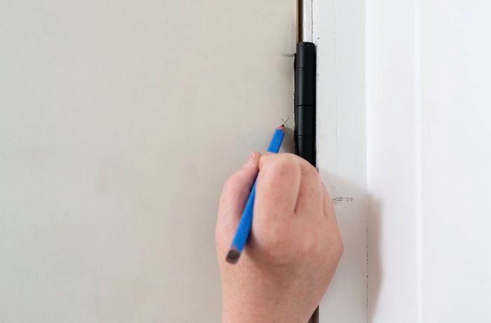 A person is marking precise hinge positions on the door edge to prepare for cutting recesses and secure hinge installation.