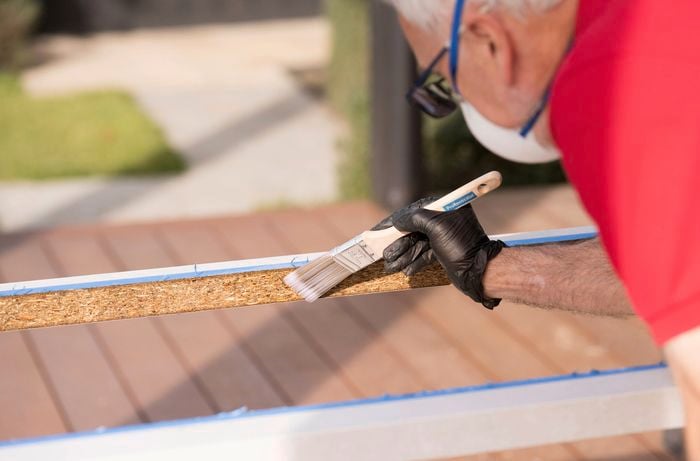 A person is sealing the raw edges of a cut benchtop with a protective coating using a paintbrush.