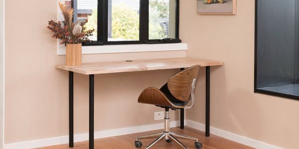 A room with a desk, chair, window, and a flower vase on the desk 