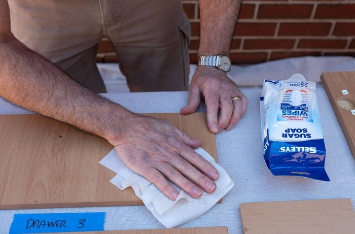 A person is cleaning the kitchen laminate cabinet drawer surface with sugar soap wipes