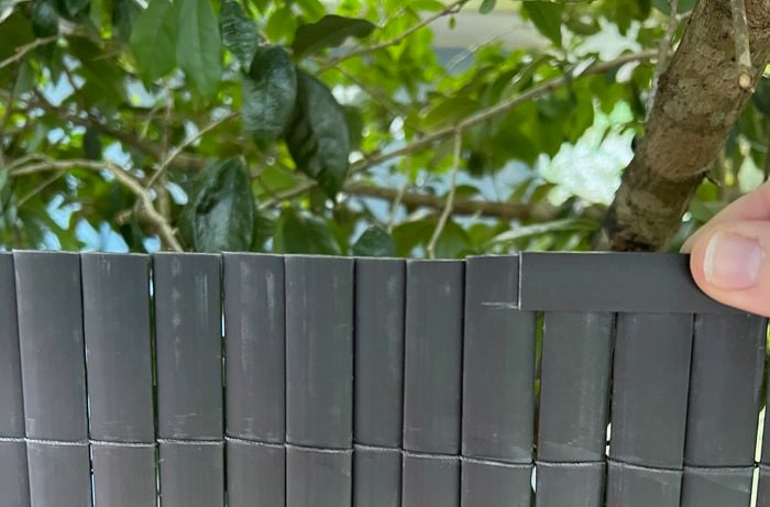 Hand holding the cords of a black fence in an outdoor background