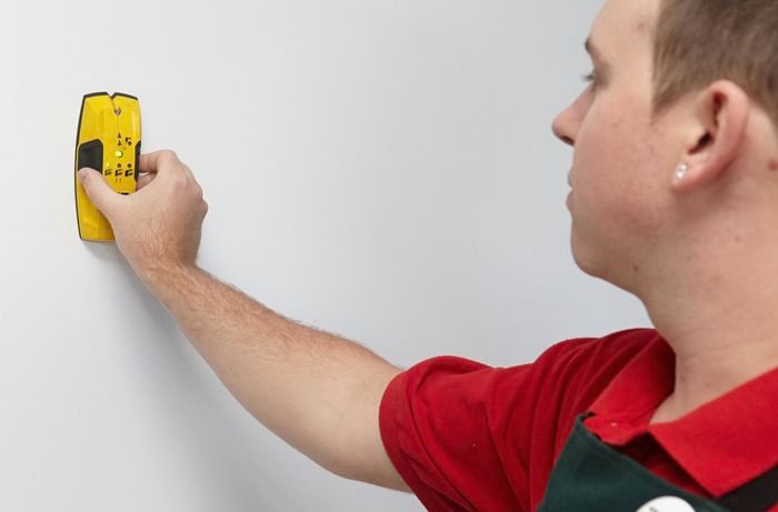 A person holding a stud finder on a plaster wall