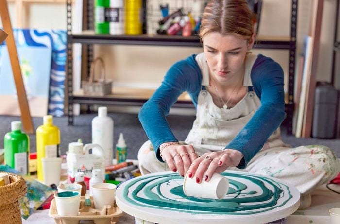 Bella in an art studio pouring light teal paint onto round canvas