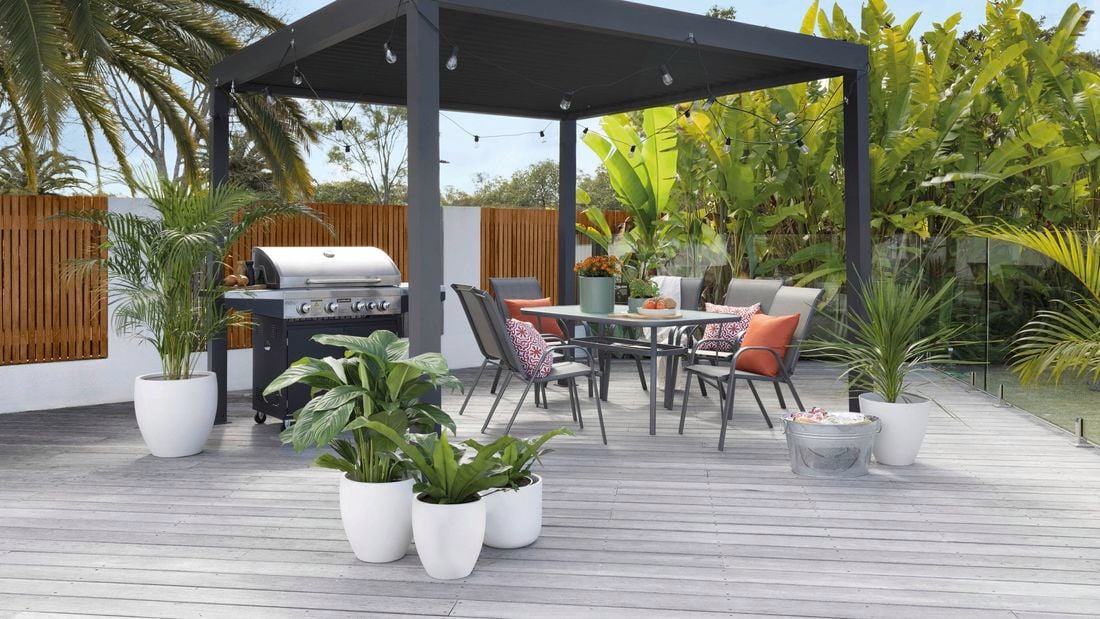 Gazibo with outdoor chairs, table, plants, barbeque and lights.