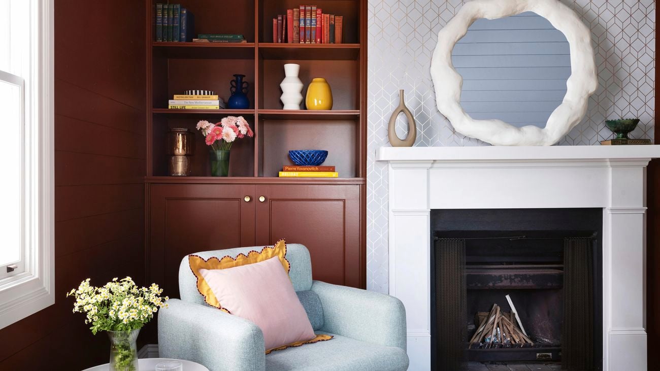 Cloud mirror sitting on the mantel of a white, woodburning fireplace, blue armchair in the foreground and with yellow flowers in vase on top of a side table next to it.