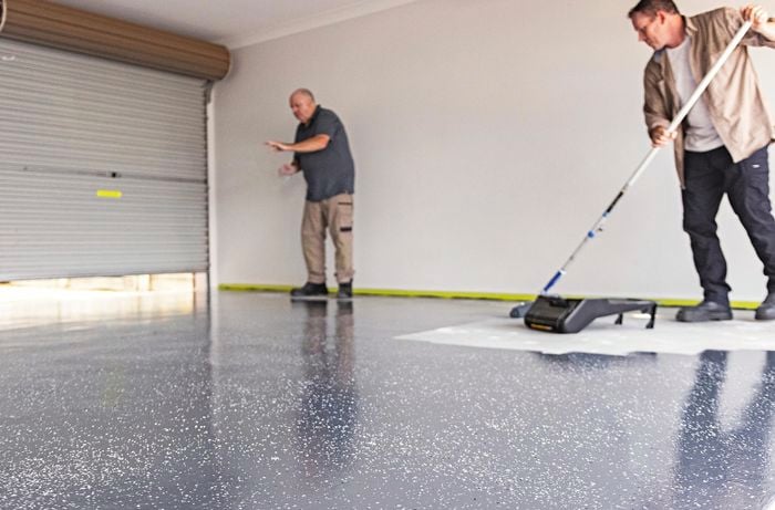  Two men in a garage, one man uses a roller to paint Dy-Mark epoxy over a garage floor