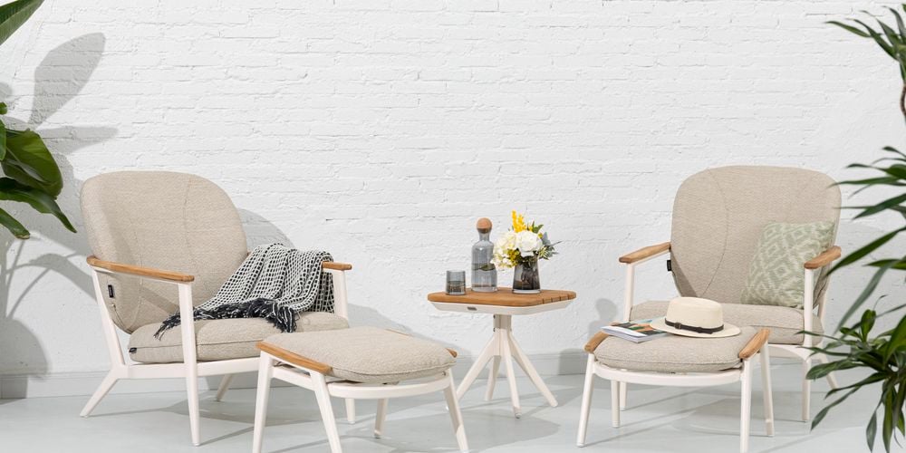 An outdoor lounge setting with aluminium chairs, footstools and a teak side table