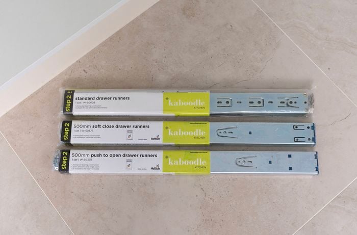The image shows three types of drawer runners including standard, soft close, and push-to-open are arranged on a tiled floor