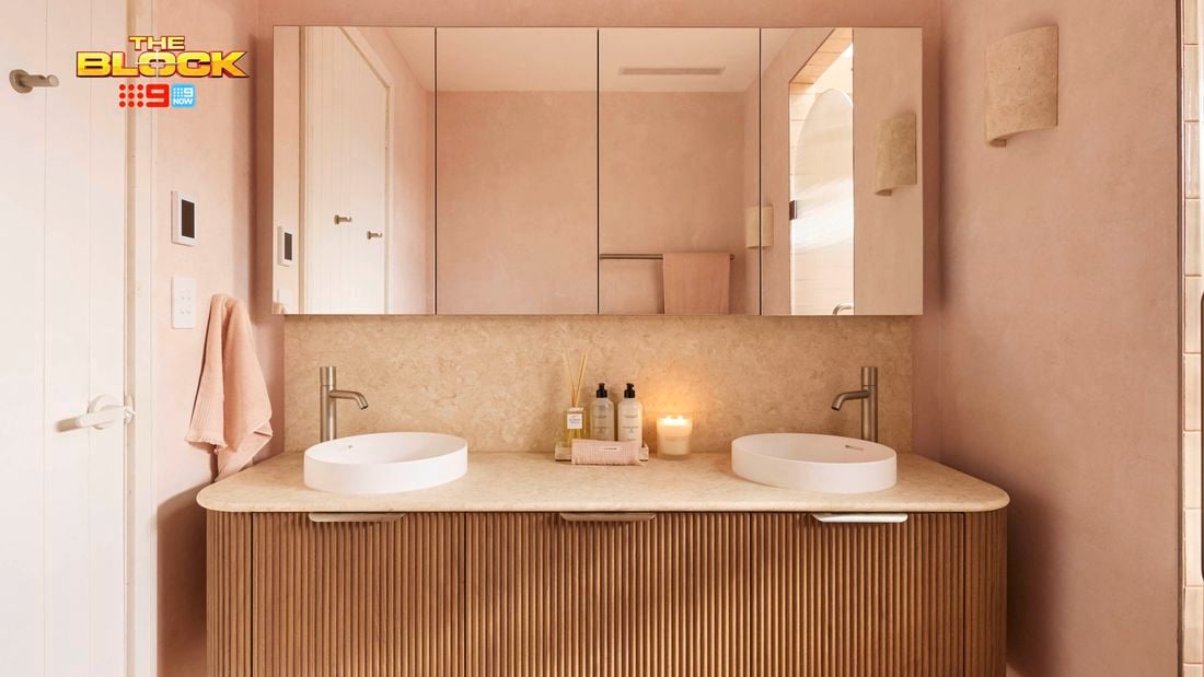 Modern bathroom with double round sinks, chrome faucets, mirrored cabinets, soft pink walls, and toiletries on the vanity. 