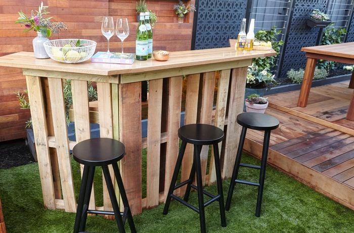 A completed wooden pallet wine bar in an outdoor entertaining area, with two bottles of beer, two wine glasses, and two bottles of Pellegrino