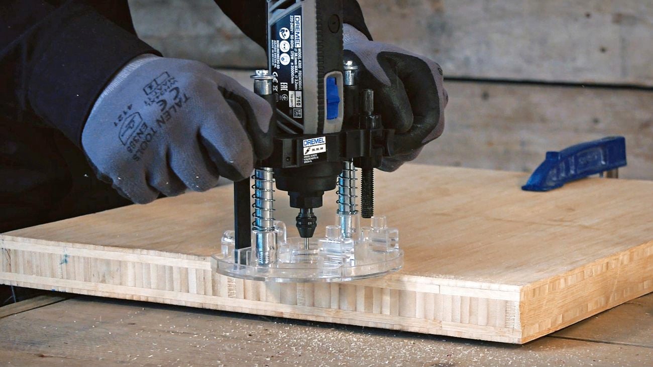 A person using a Dremel rotary tool and plunge router accessory.