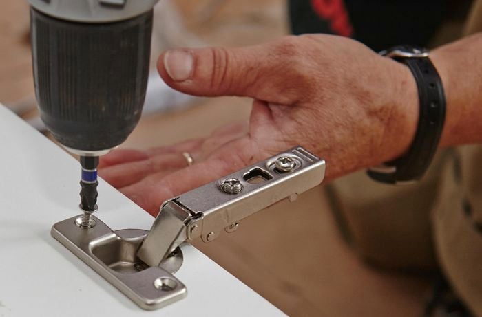 Screwing in a hinge into the pre-drilled holes
