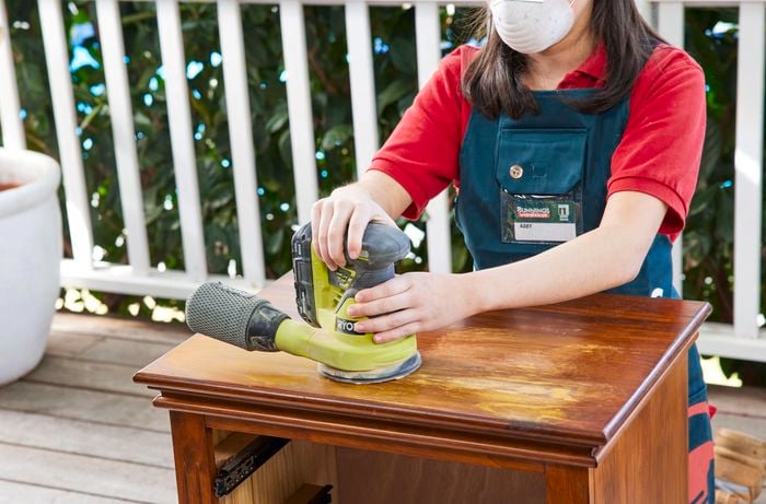 Person using an orbital sander to sand the top of the bedside table.