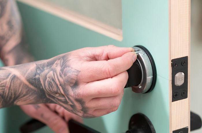 A person is securing a rivet into the lock cylinder on a door to ensure the lock stays firmly and prevent movement.