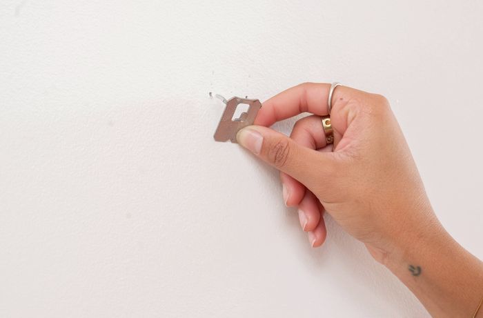 Image Description: A person is installing a claw picture hanger at the marked spot on a plasterboard wall and checks that it sits firmly against the surface before hanging any weight. 