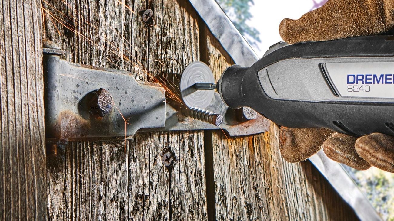 A Dremel rotary tool cuts through a metal bolt in a wooden fence