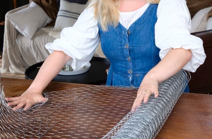 Lady rolling out wire netting on wooden table.