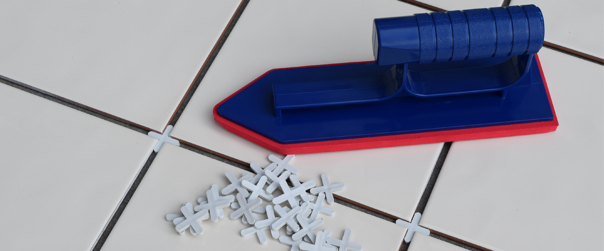 Close up of a blue grouting float and plastic tile spacers sitting on white tiles