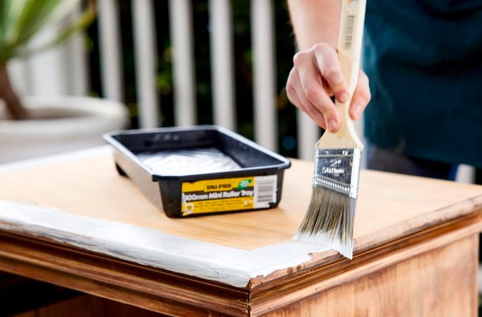 Person applying primer with a paintbrush to the edges of the bedside table.