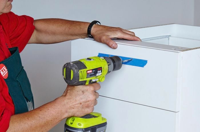 A person drilling a hole in a drawer front using a cordless drill