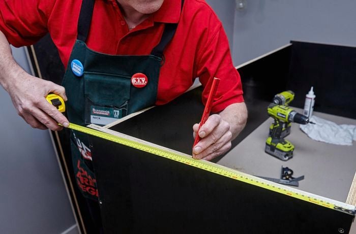 Person measuring and marking the centre of a piece of timber using tape measure and pencil