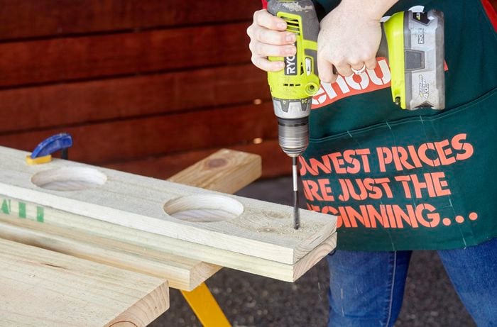 A person drilling a hole into the end of a pine board